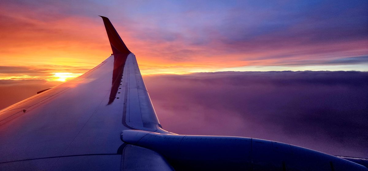 An airplane wingtip against a purple and orange sunset