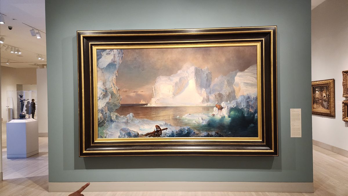 A large framed seascape painting hanging in an art museum gallery