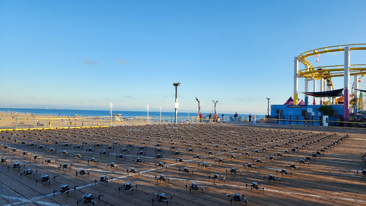 A beach drone launch site with drones in rows near a pier at golden hour