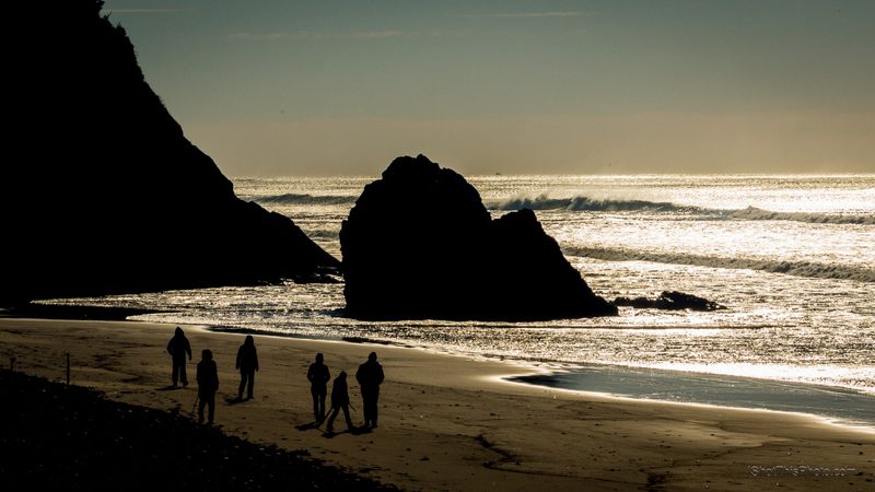 People walking a glowing beach beneath dark sea stacks at sunset
