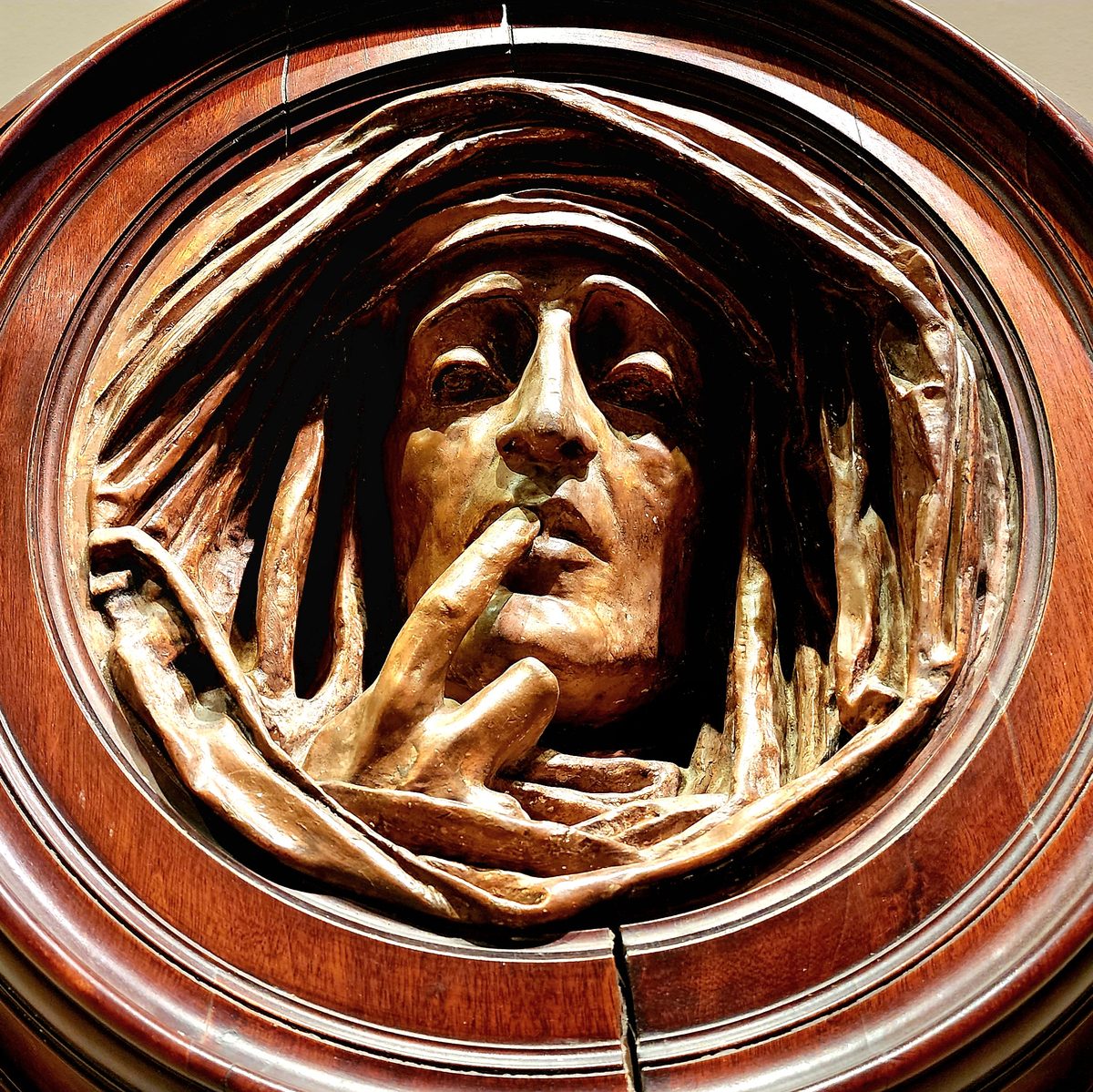 A carved bronze medallion of a pensive face with a hand at its chin