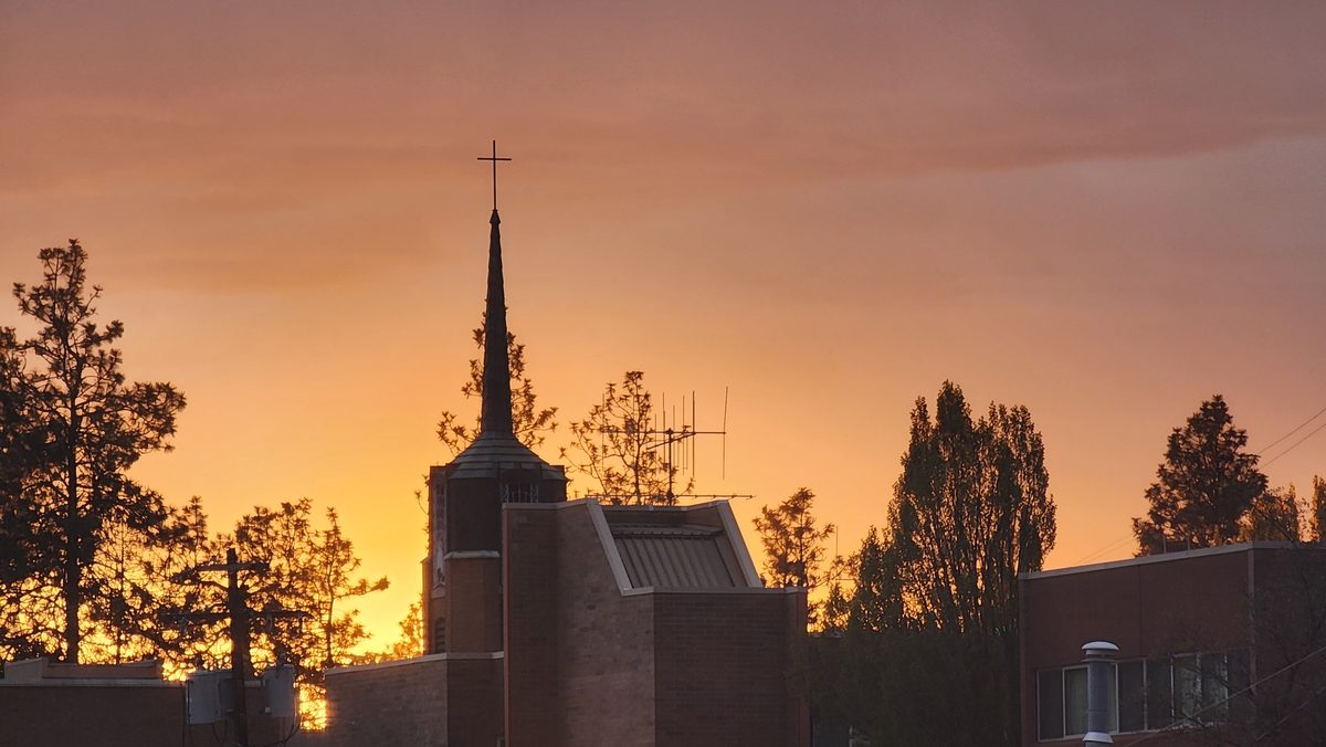 A church steeple and trees silhouetted against an orange sunset