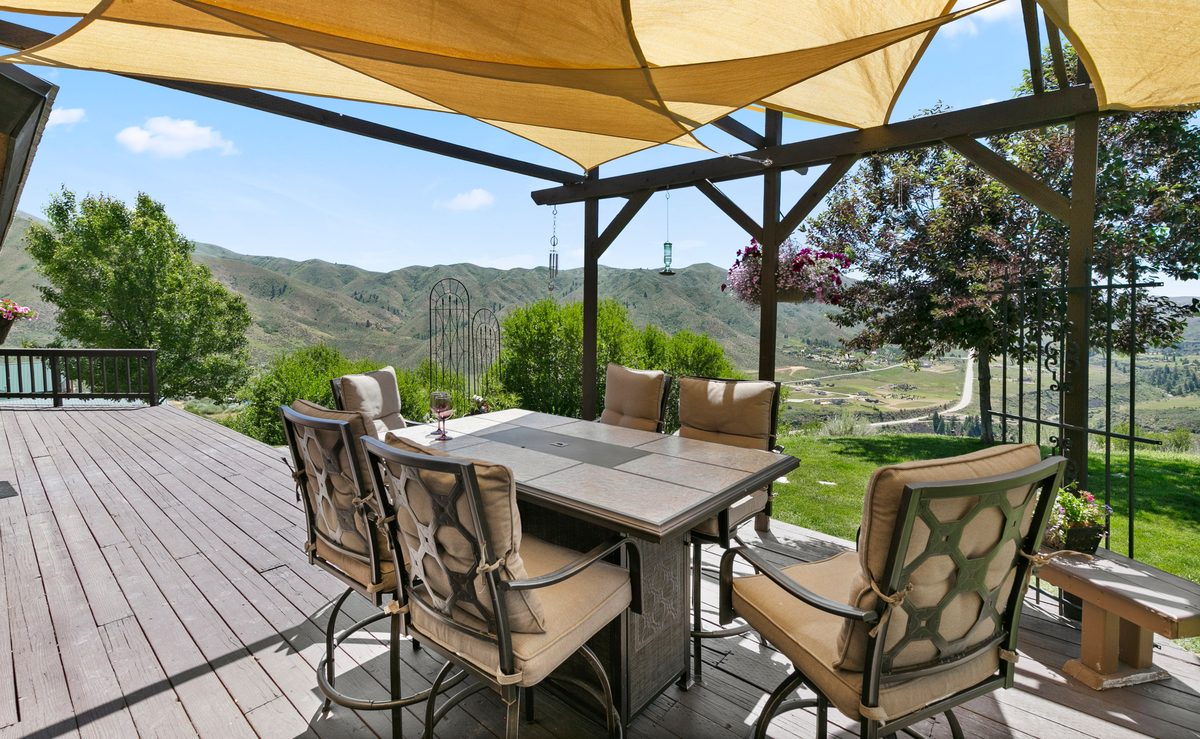 Covered patio dining set under a shade sail with green hills beyond
