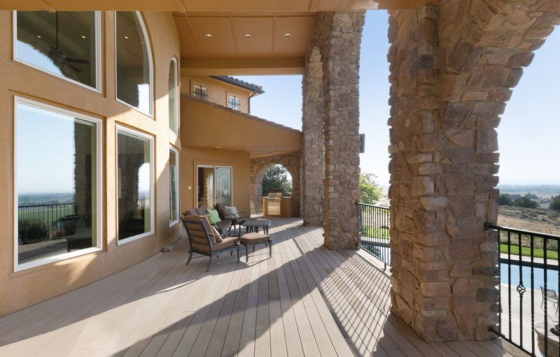 Covered balcony with stone columns, arched windows, patio chairs and a railing over the valley.