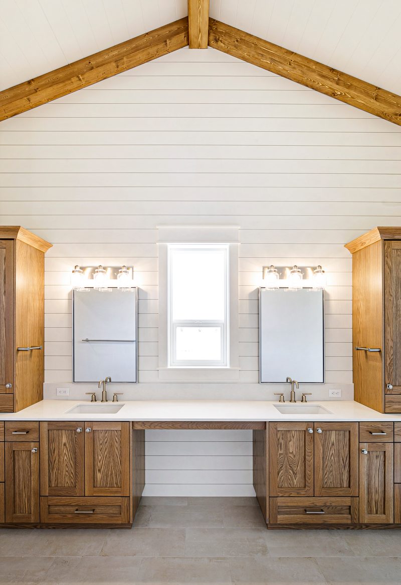 Bathroom double vanity in natural wood under a vaulted ceiling with a timber beam