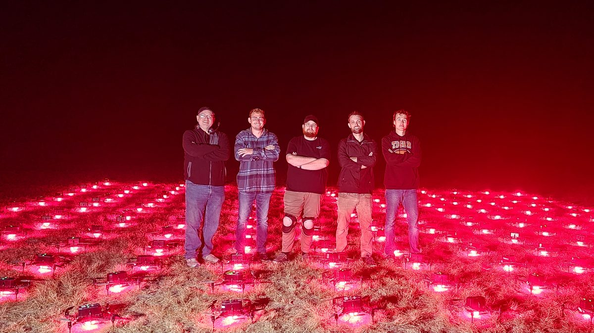 A drone show crew standing in a field of red-lit drones at night