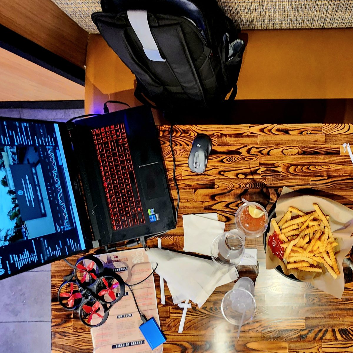 A laptop, FPV drone, coffee and fries on a busy work table