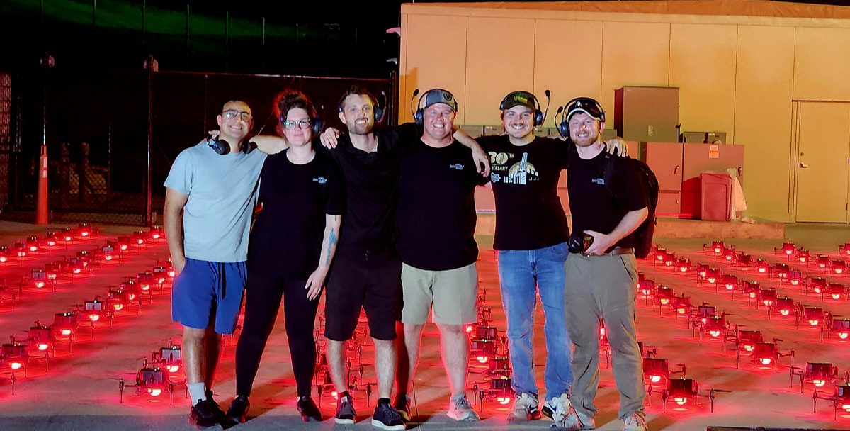 A drone show crew posing in front of hundreds of red-lit drones