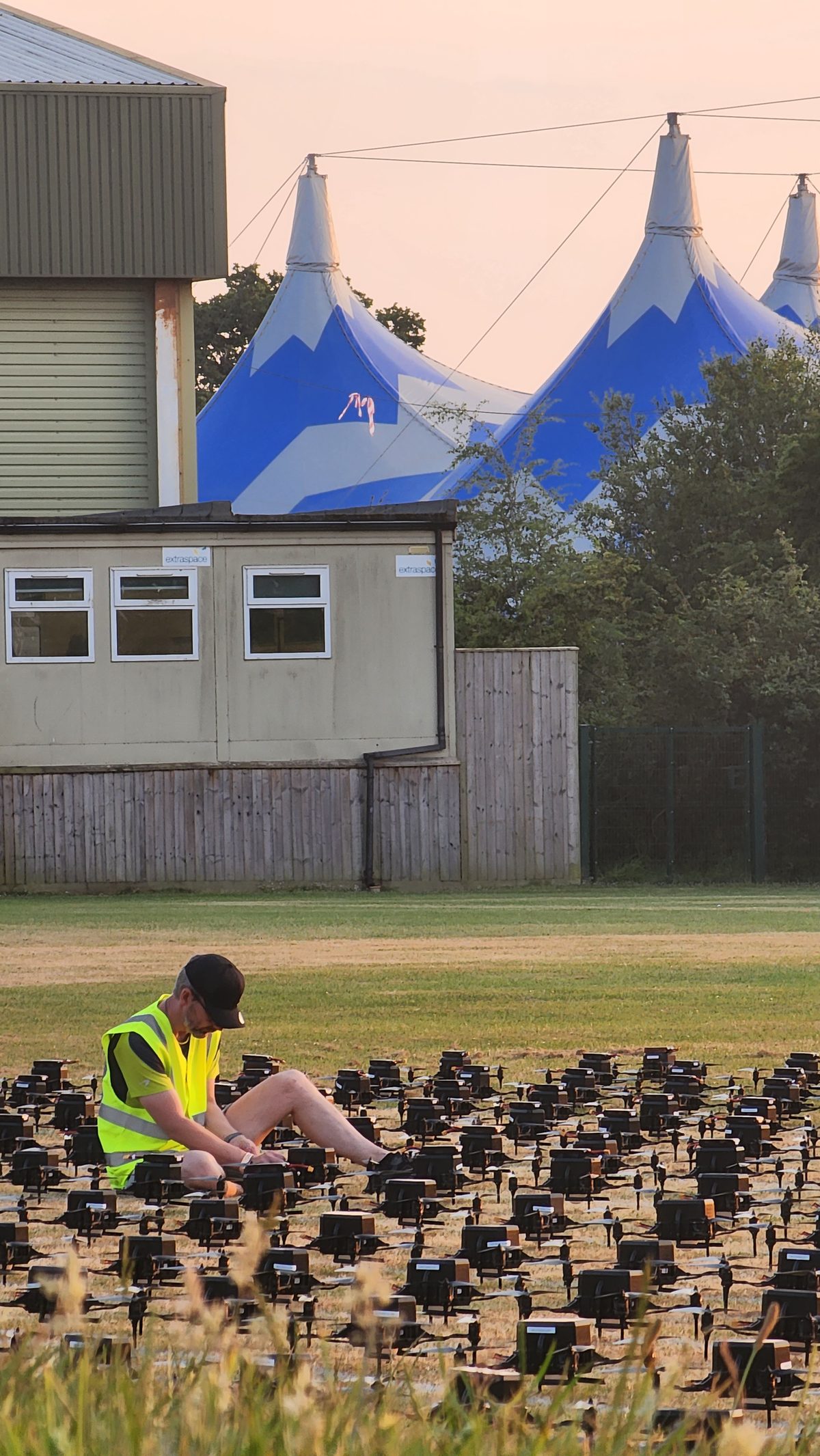 Drones lined up on grass beside blue festival tents