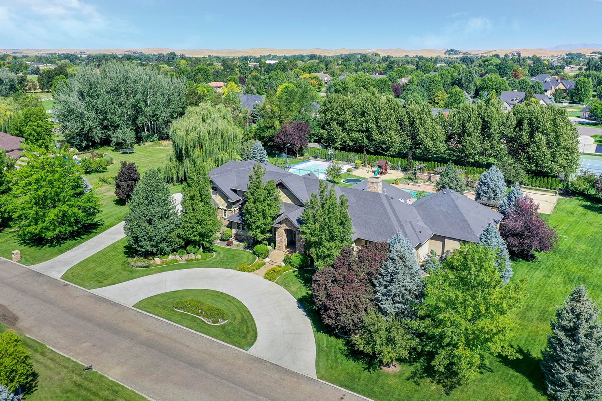 Drone photo of a large home on wooded acreage with a circular driveway and lawn