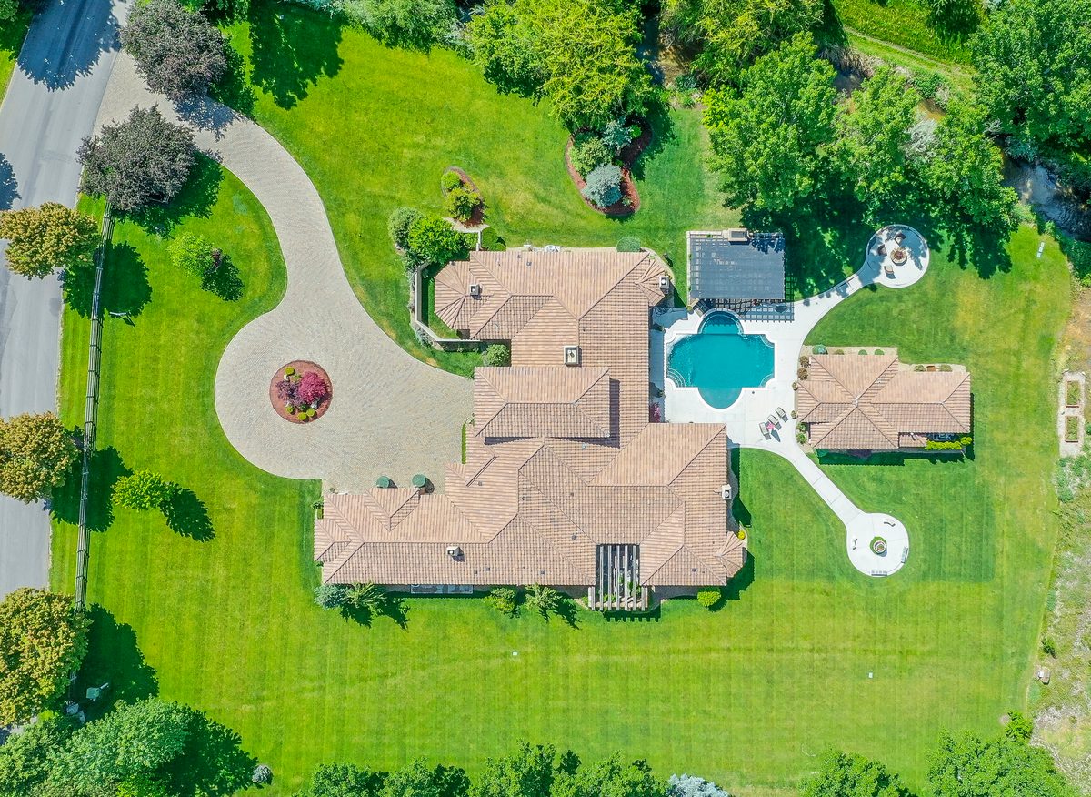 Top-down drone photo of a large tile-roof estate home with a pool, circular driveway and mature trees