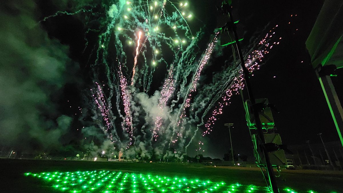 Green fireworks bursting above a field of glowing green drones