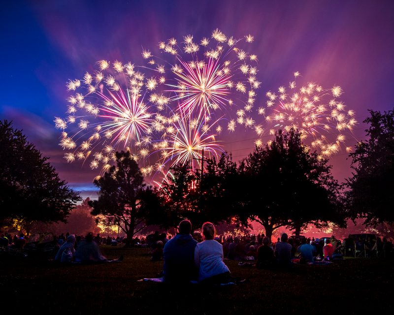 Pink and gold fireworks bursting above silhouetted trees and a crowd at night
