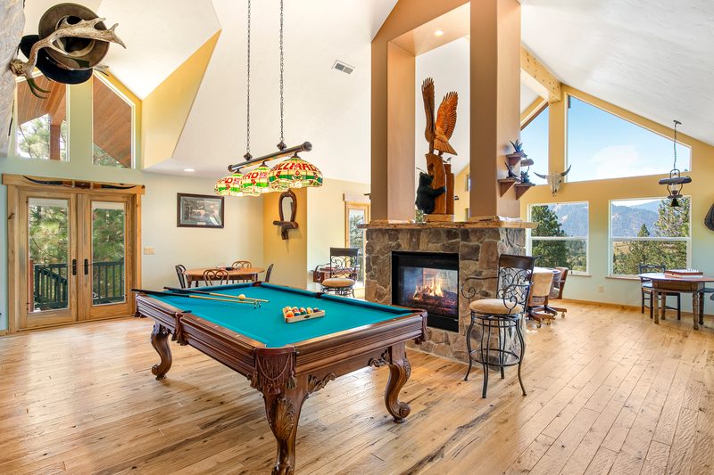 Vaulted game room with a pool table, stone fireplace, timber beams and a mounted moose head