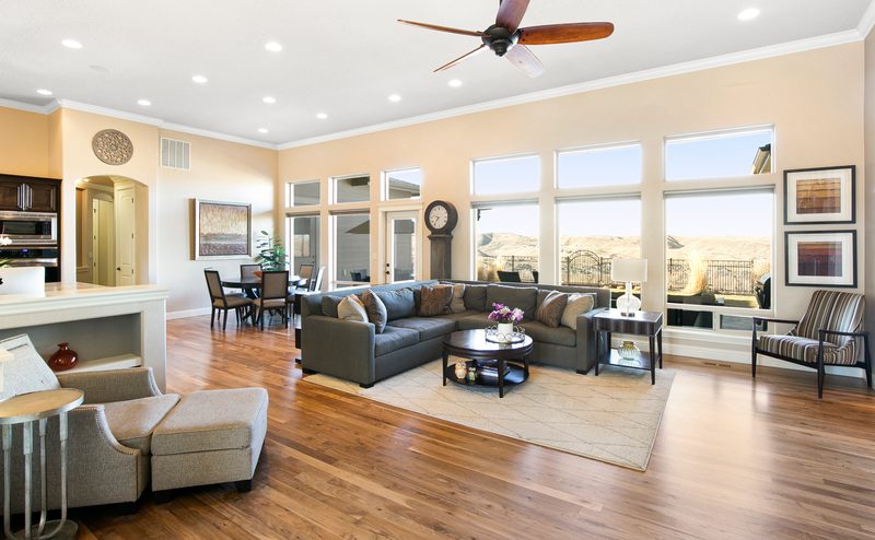 Open great room with a sectional sofa, ceiling fan and a long wall of windows