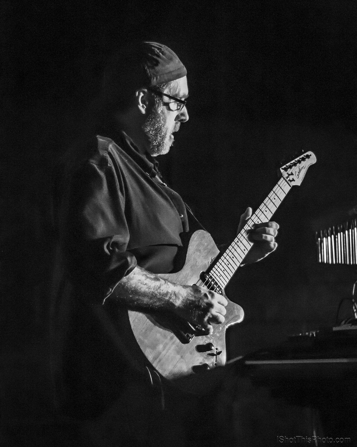Low-key photo of a guitarist in a cap playing a white electric guitar at the Crazy Horse