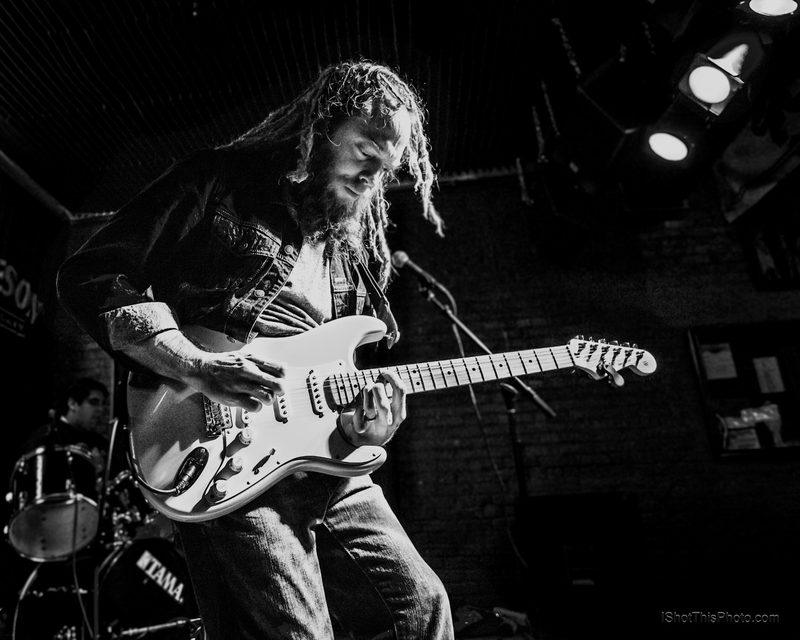 Black-and-white photo of a long-haired guitarist playing a Stratocaster under stage lights