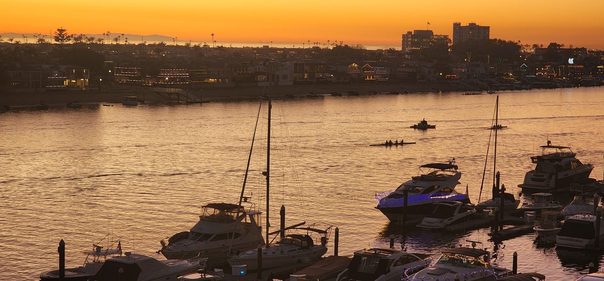 Boats moored in a calm harbor under an orange dusk sky