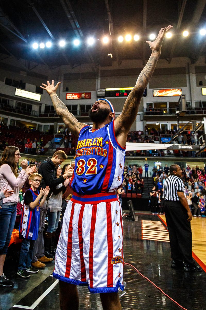 A Harlem Globetrotters player raising both arms to the arena lights to pump up the crowd