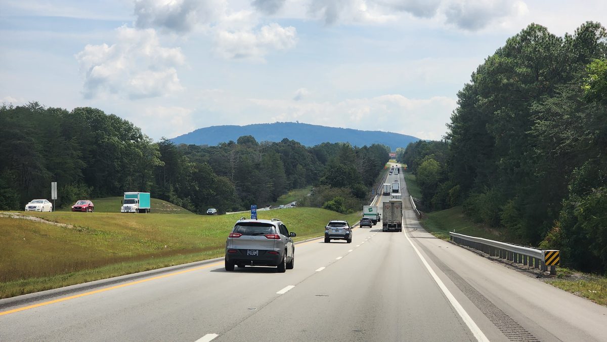A divided highway stretching toward wooded hills under a cloudy sky
