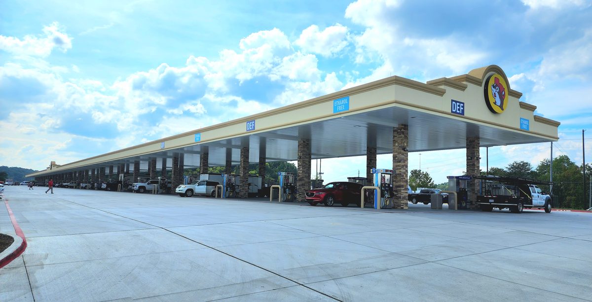 A large highway travel center fuel canopy under a blue sky with puffy clouds