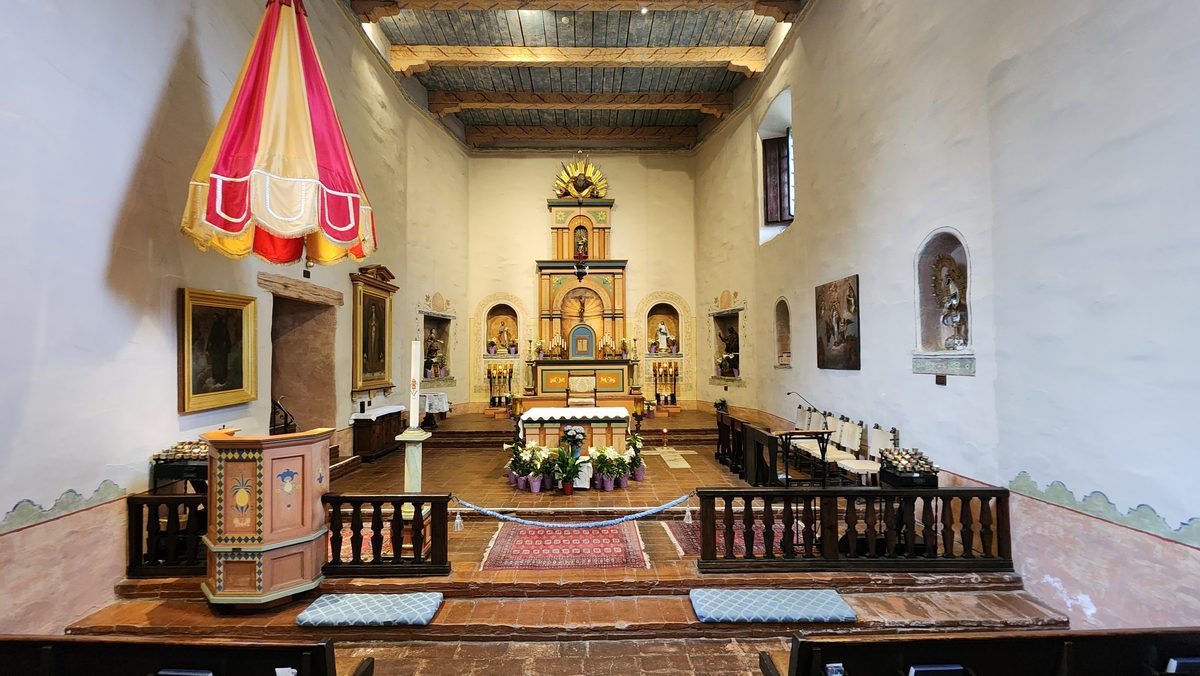 Interior of a historic Spanish mission chapel with a gilded altar and painted beams