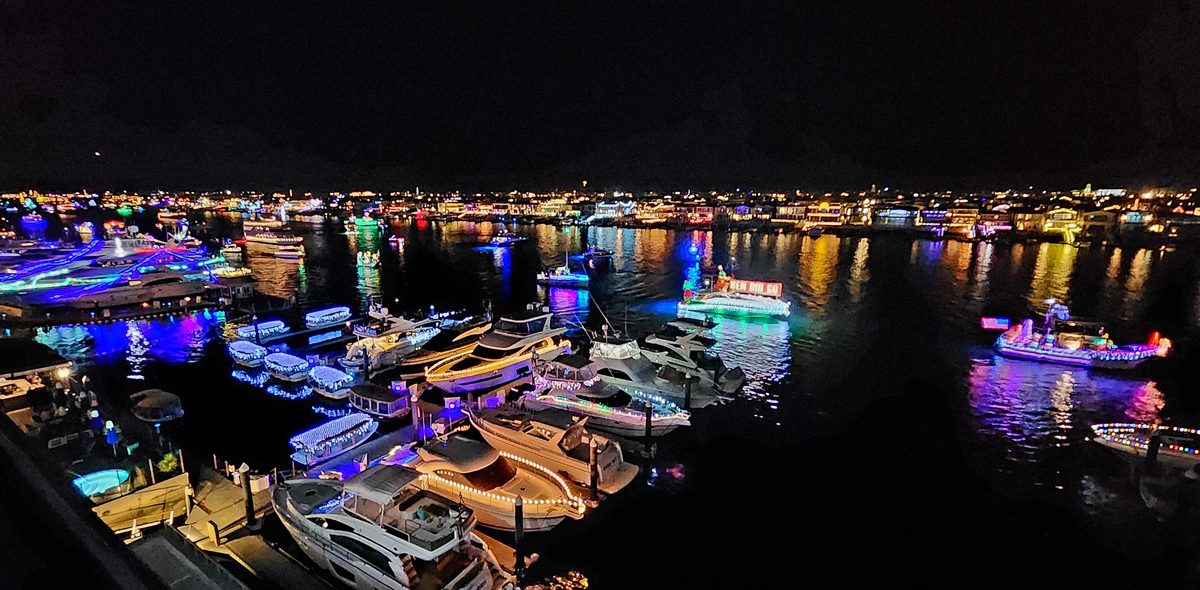 Boats covered in holiday lights reflecting on the harbor at night