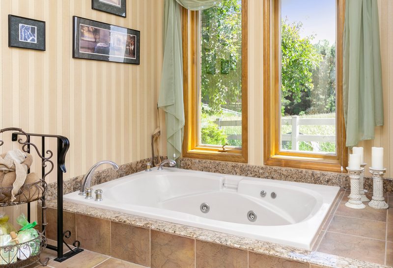 Corner jetted tub with window views of a green yard and trees