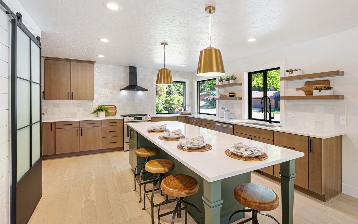 Bright kitchen with floating shelves, gold pendants and a long island with stools
