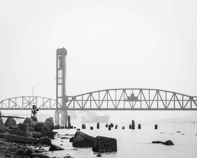 Black-and-white photo of a steel lift bridge and pilings fading into thick fog