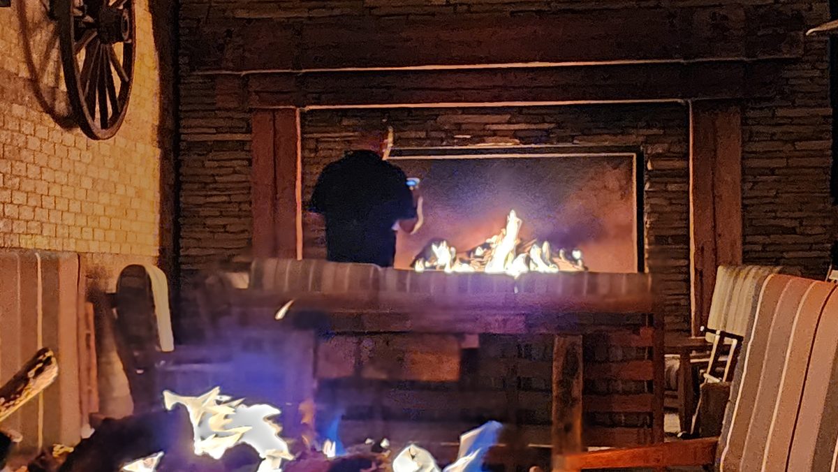 A man standing by a roaring lodge fireplace late at night
