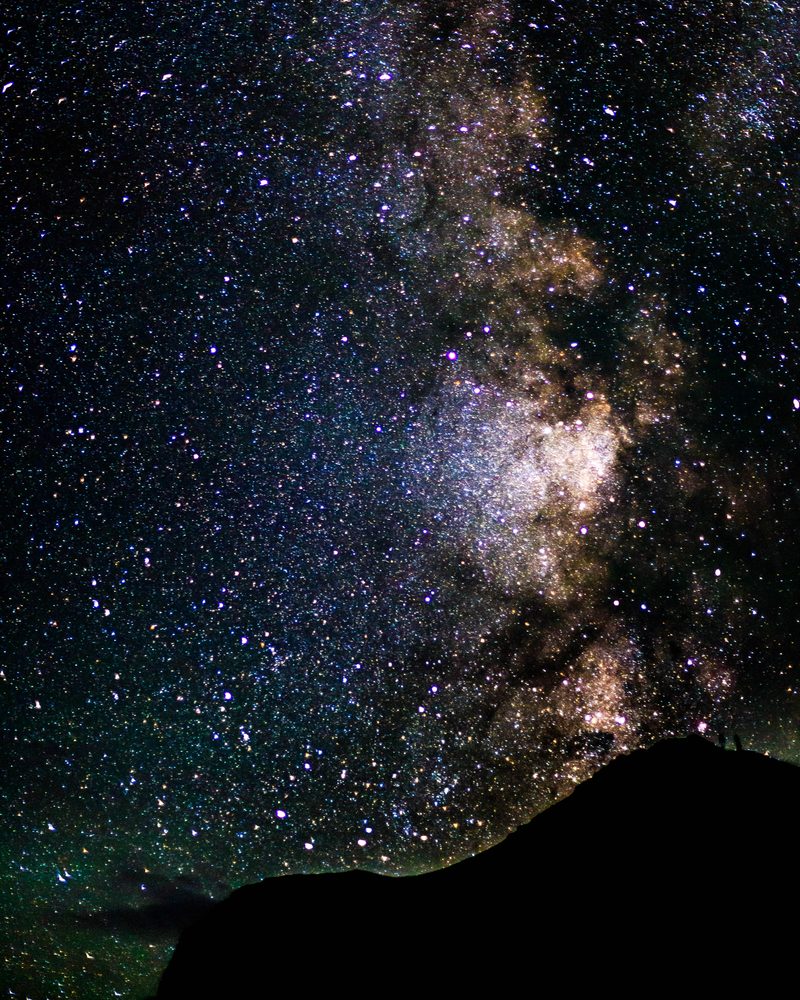A dense Milky Way core rises over a black mountain ridge in a star-filled sky.
