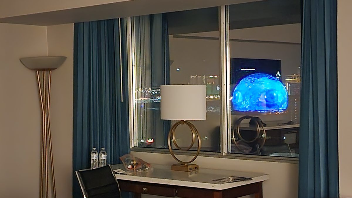 A modern hotel room with a glowing wall screen and tall curtains