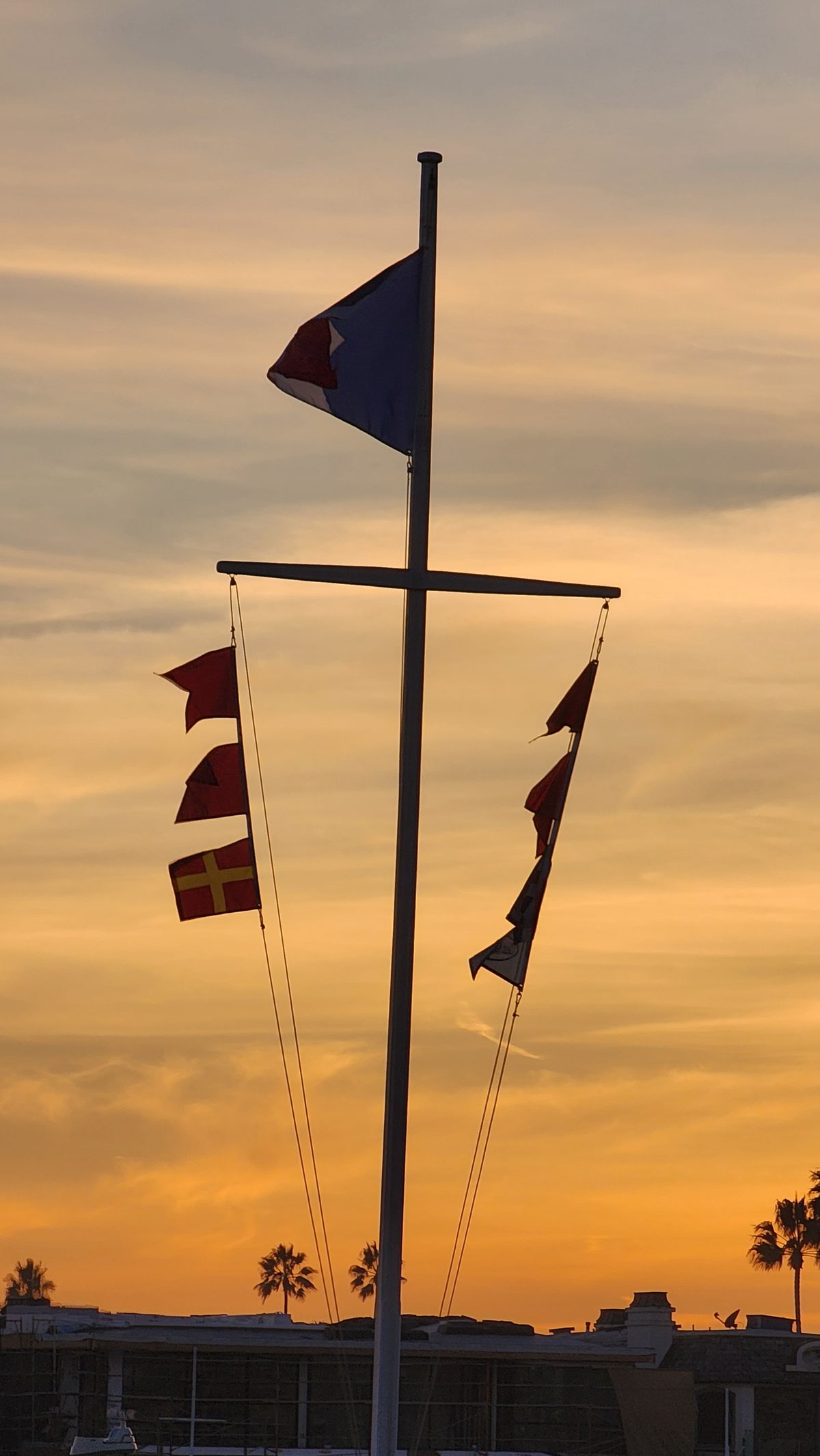 A mast of nautical signal flags silhouetted against a golden sunset