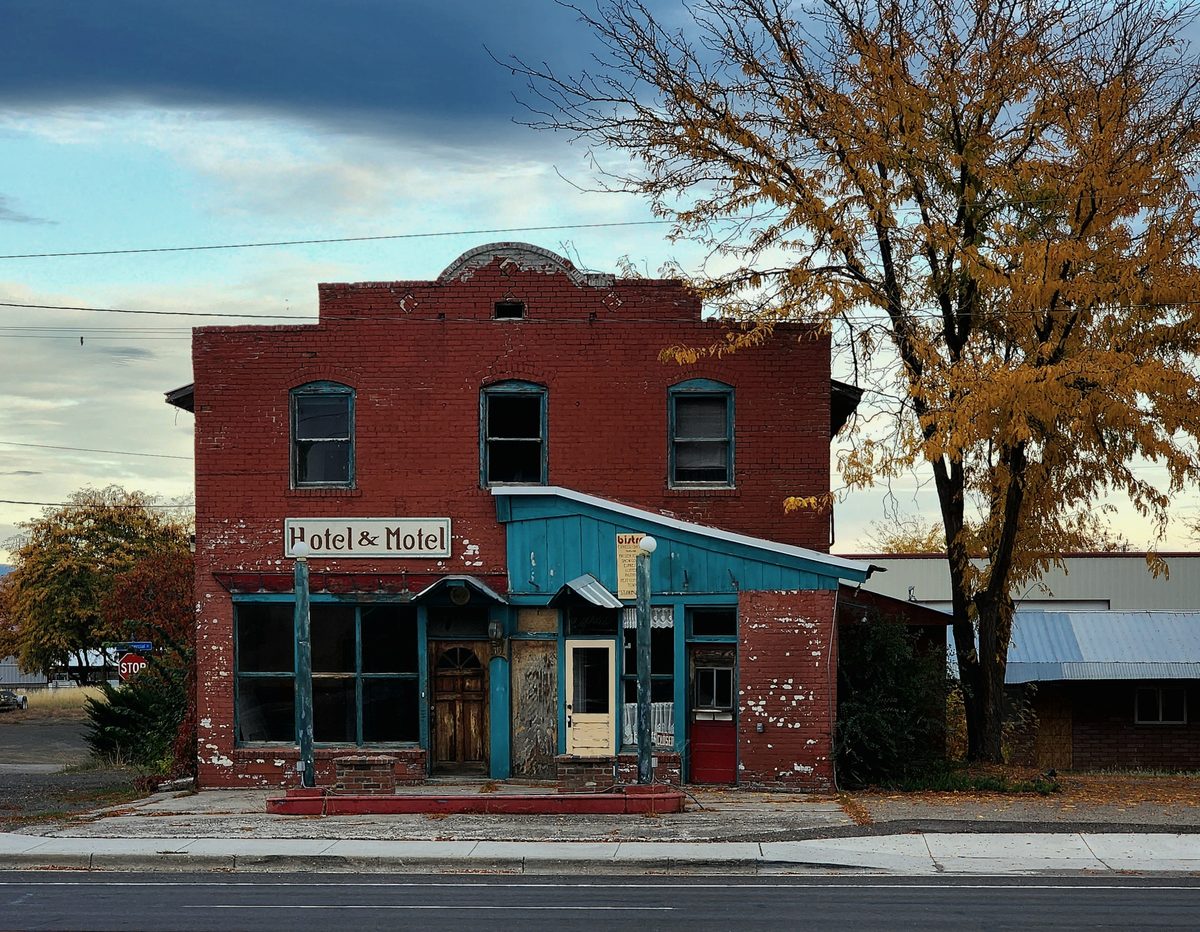 A weathered red-brick storefront beside an autumn tree at golden hour