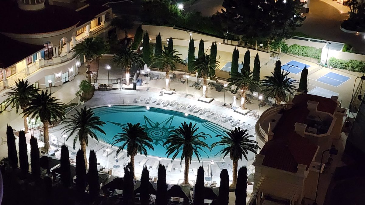 A lit resort pool and palm trees beside a hotel tower at night