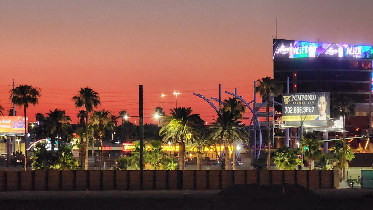 Palm silhouettes and a lit Ferris wheel under a red dusk sky