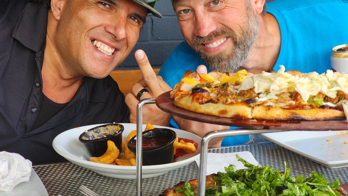 Two smiling friends with a pizza on a sunny patio