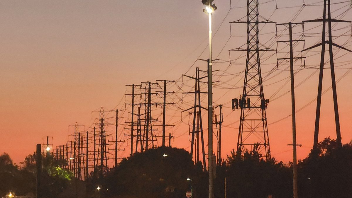 Power-line towers silhouetted against an orange sunset