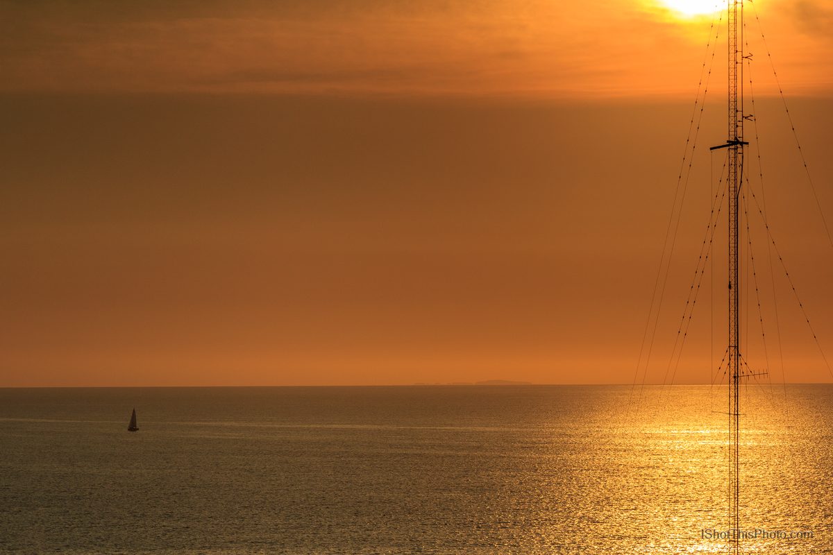 Golden sunset over the Bay of Banderas with a lone sailboat and radio mast in Puerto Vallarta