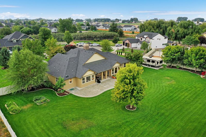 Drone photo of a ranch-style home on a large green lot with mature trees