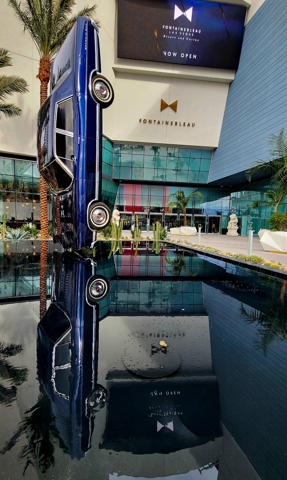 A tall resort tower reflected in a still rooftop pool