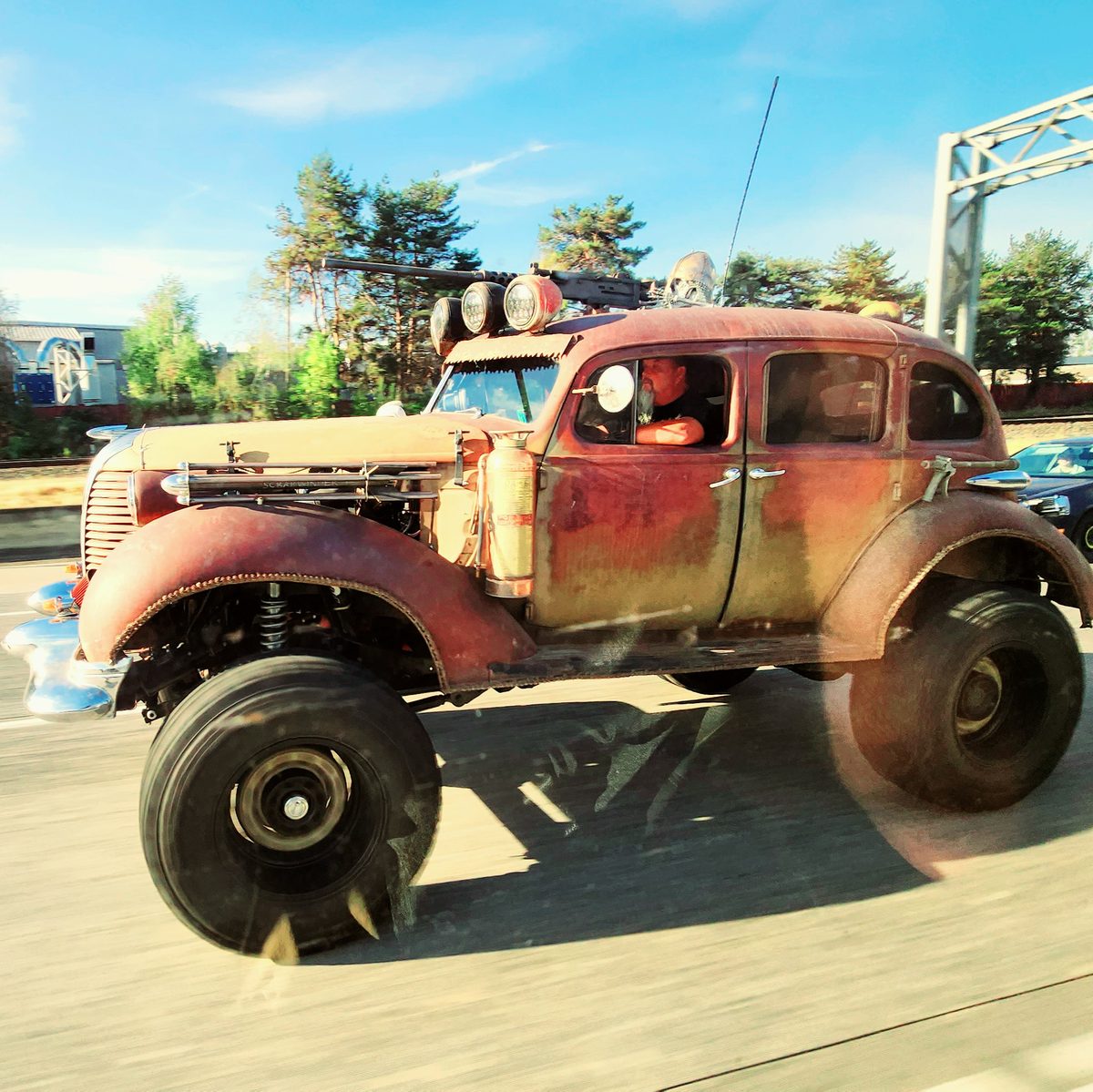 A rusty lifted classic car with huge off-road tires on a street