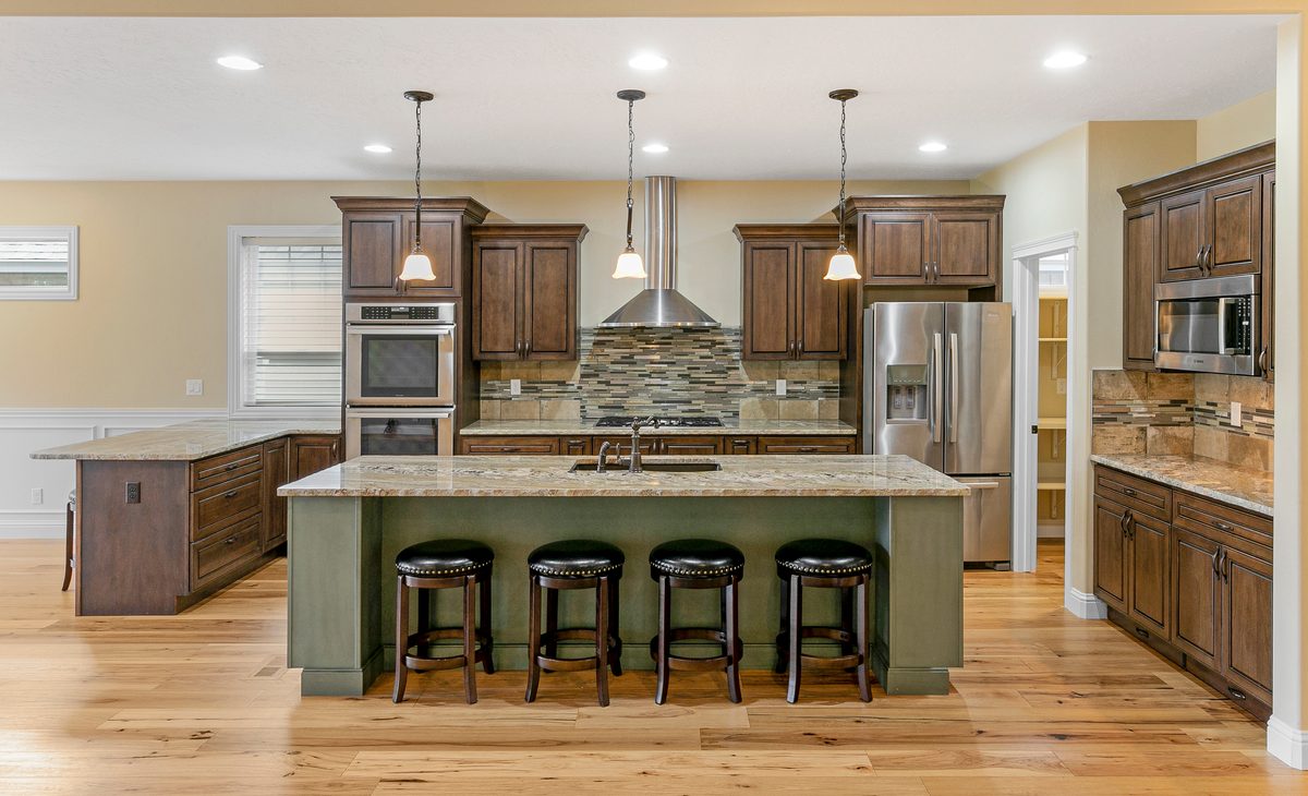 Kitchen with a sage green island, stone backsplash and black bar stools