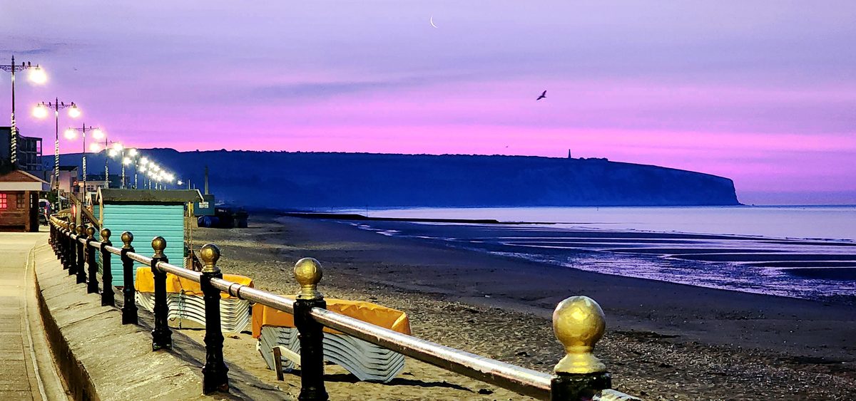 A pink dawn over a seaside promenade and white cliffs