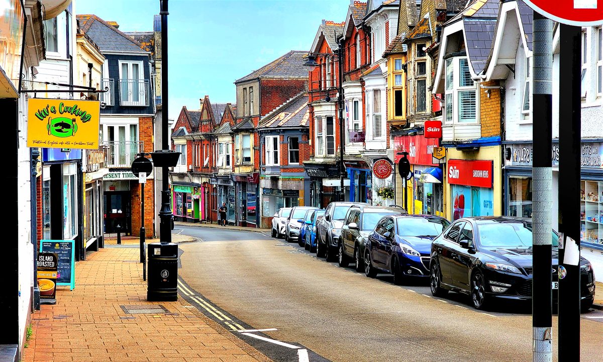 A colorful small-town high street with shopfronts and parked cars