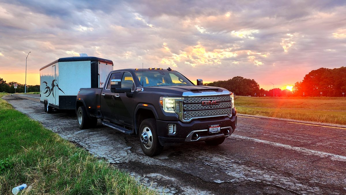 A pickup truck and equipment trailer parked on grass at sunset