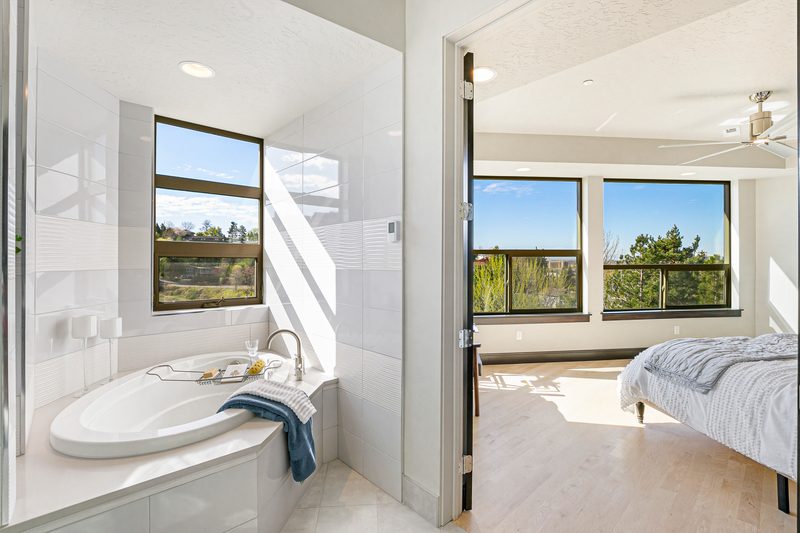 Soaking tub by a window with a view through to a bright bedroom