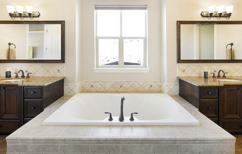 Primary bathroom with a soaking tub under a window between two dark vanities