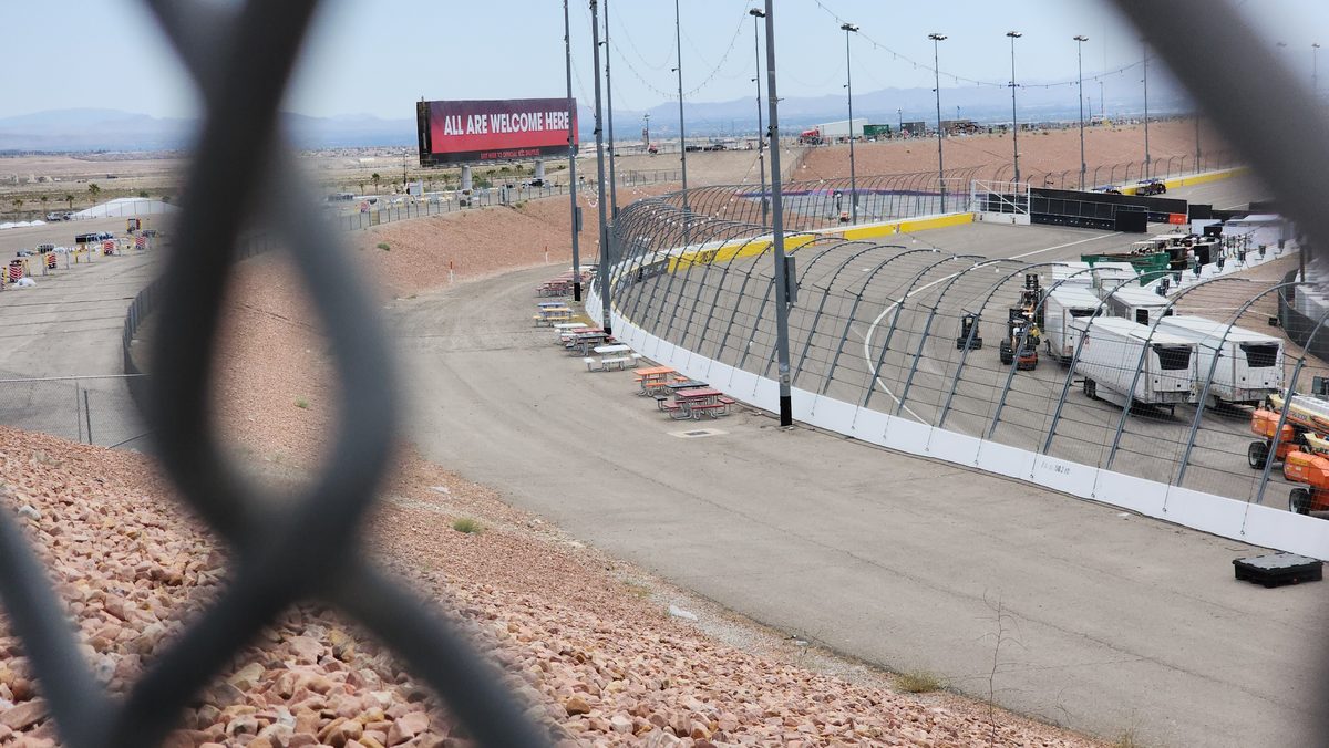 A speedway track and grandstand seen through a chain-link fence
